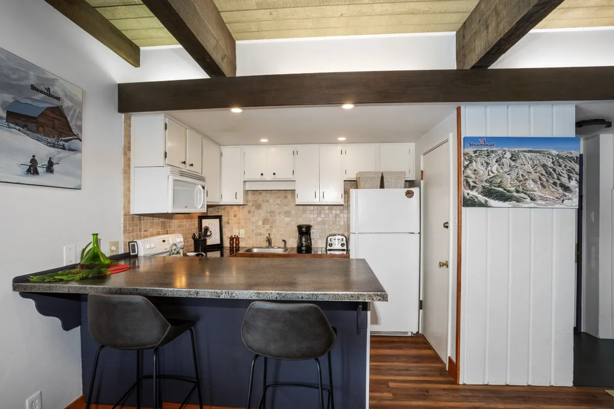 This image captures the heart of the newly renovated kitchen, focusing on a spacious kitchen island with stylish bar stools, modern appliances, and tasteful wall artwork. The space appears open, with clear sightlines into adjacent living areas, suggesting ease of socializing and connection while cooking or dining.