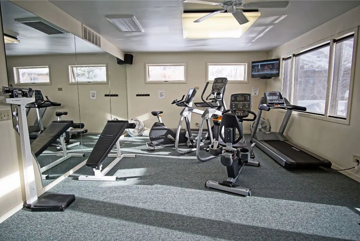 A bright, well-equipped fitness center with various exercise machines and free weights, enhanced by natural light streaming through the windows and mirrored walls that amplify the space. The atmosphere is energetic and motivating, inviting guests to keep up with their routines even while away from home.