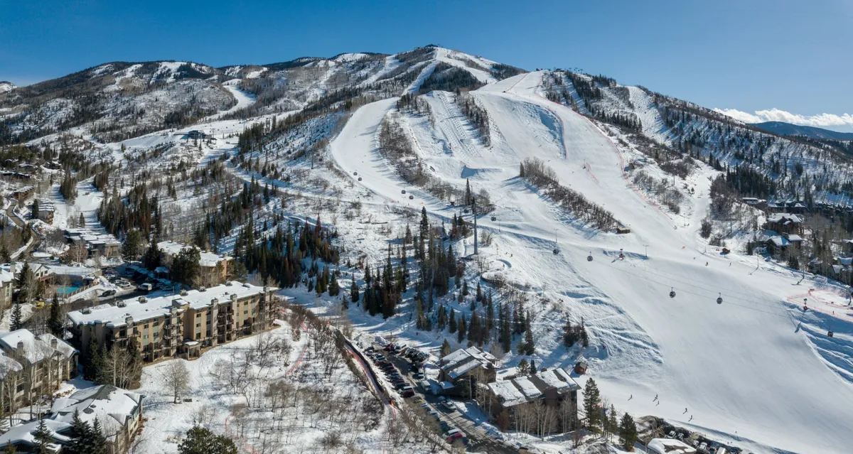 A panoramic exterior view of snow-covered slopes, ski lifts, and residential buildings set against a stunning mountain range. The scene is filled with excitement, showing both the direct proximity to the slopes and the inviting environment for skiers and snowboarders.