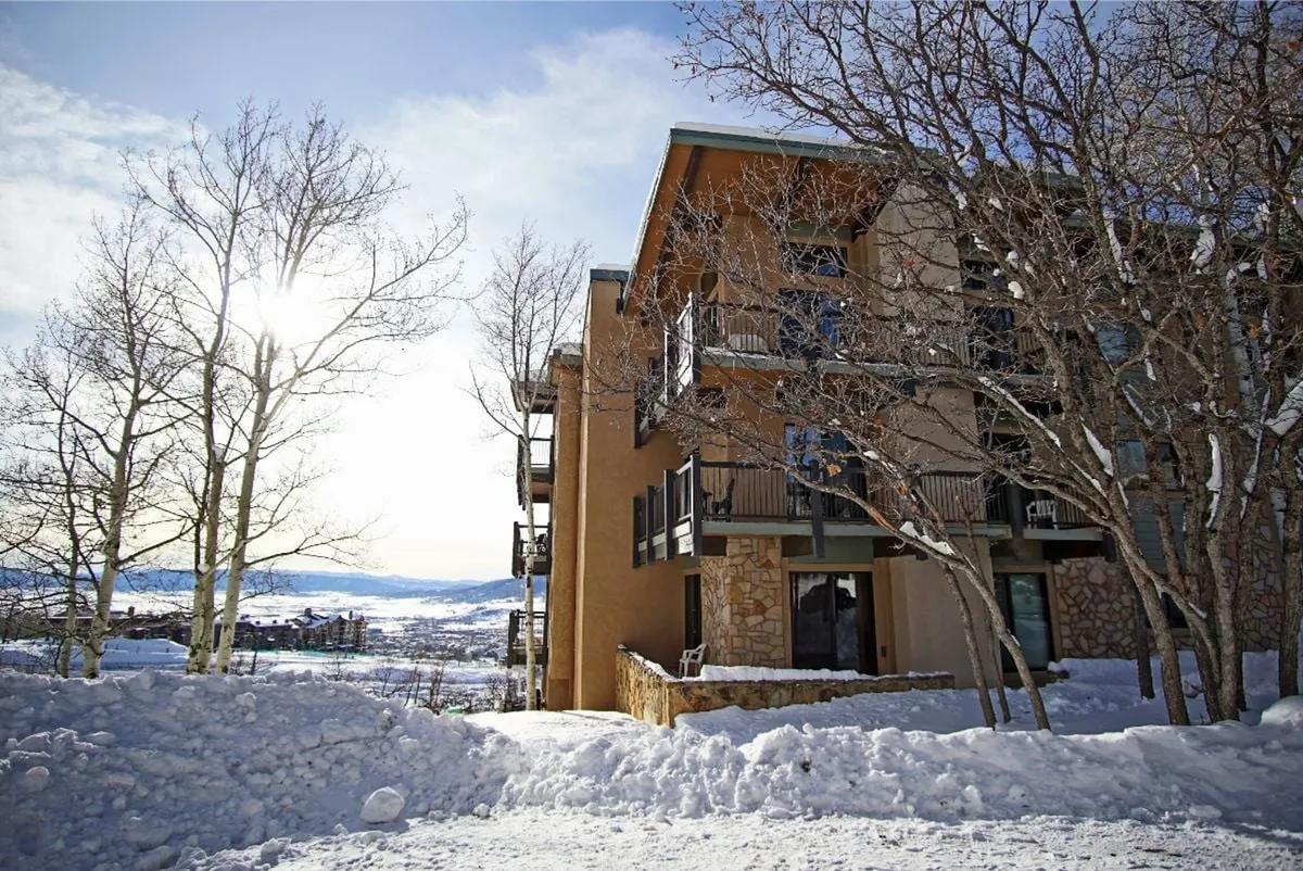 This exterior image shows the building surrounded by snow-covered ground and bare trees, with a mountain view visible in the background. The scene evokes a sense of peace and accessibility, highlighting the property's proximity to natural beauty and outdoor recreation.