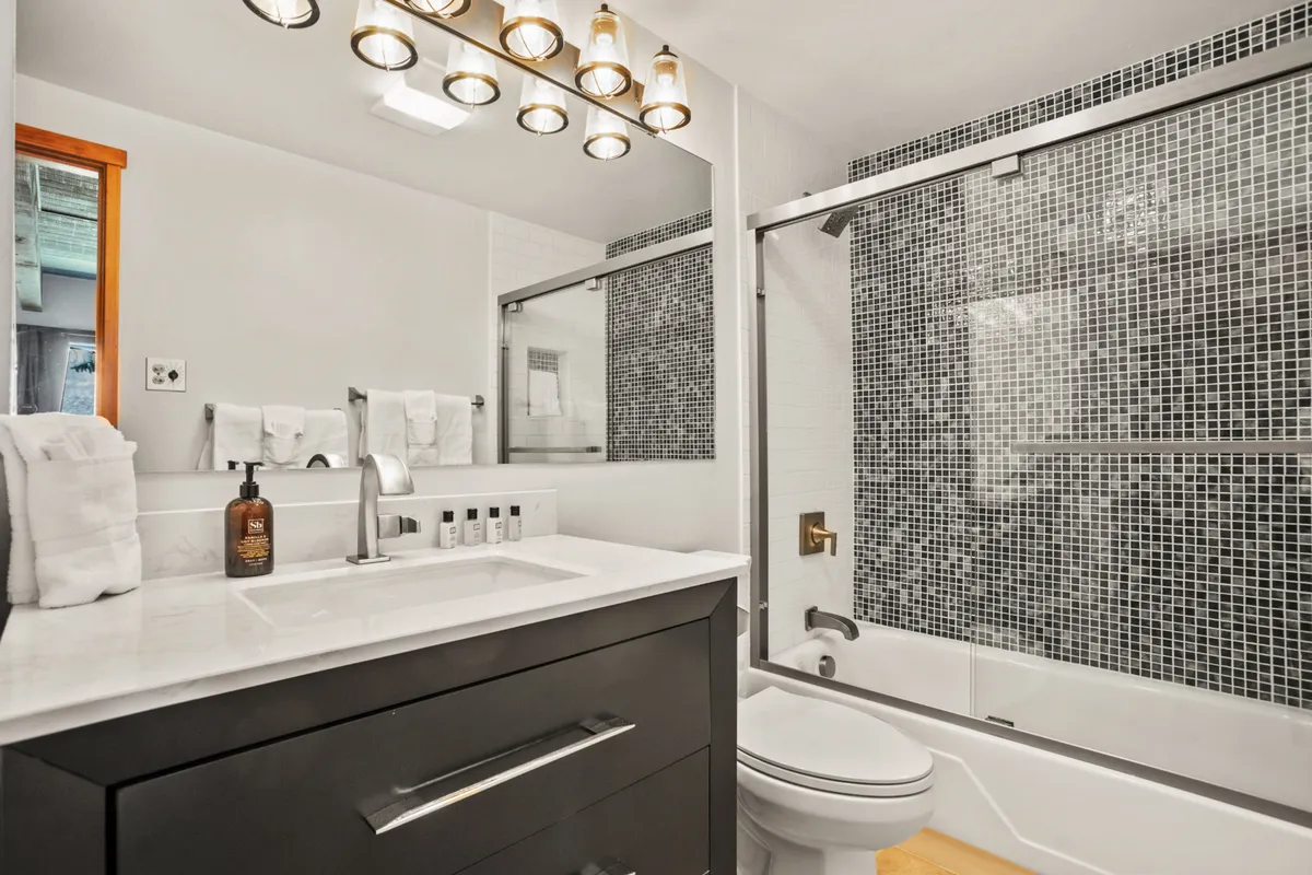 A contemporary bathroom with a sleek vanity, spacious mirror, light fixture, and a modern shower area. The clean design and sophisticated touches evoke a spa-inspired atmosphere, perfect for unwinding after outdoor activities.