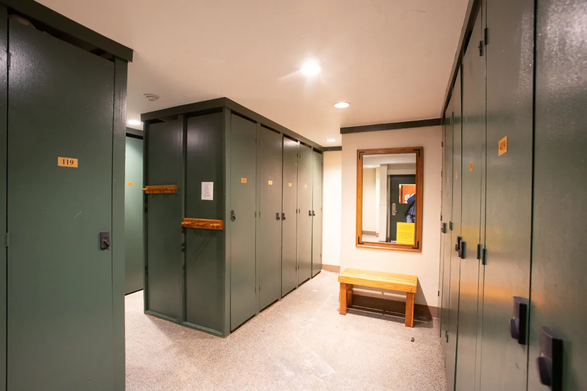 An interior view of a heated ski locker room with lockers, a bench, and a mirror. The space is functional yet inviting, providing a glimpse of the practical amenities that make the ski-in/ski-out lifestyle effortless.