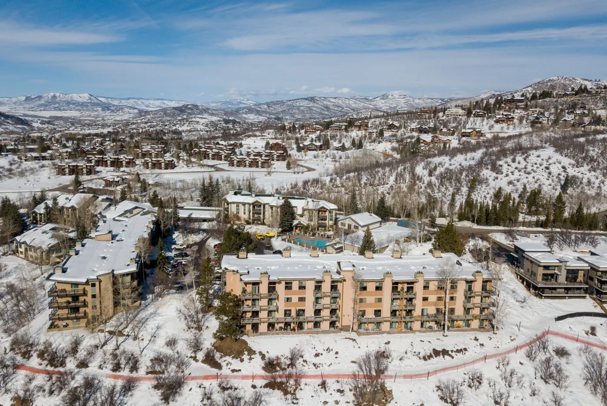 This exterior shot captures the condominium buildings framed by mountains and a prominent swimming pool area in the foreground. The pool is inviting and well-maintained, with the mountains providing a dramatic backdrop, suggesting a refreshing post-trail experience.