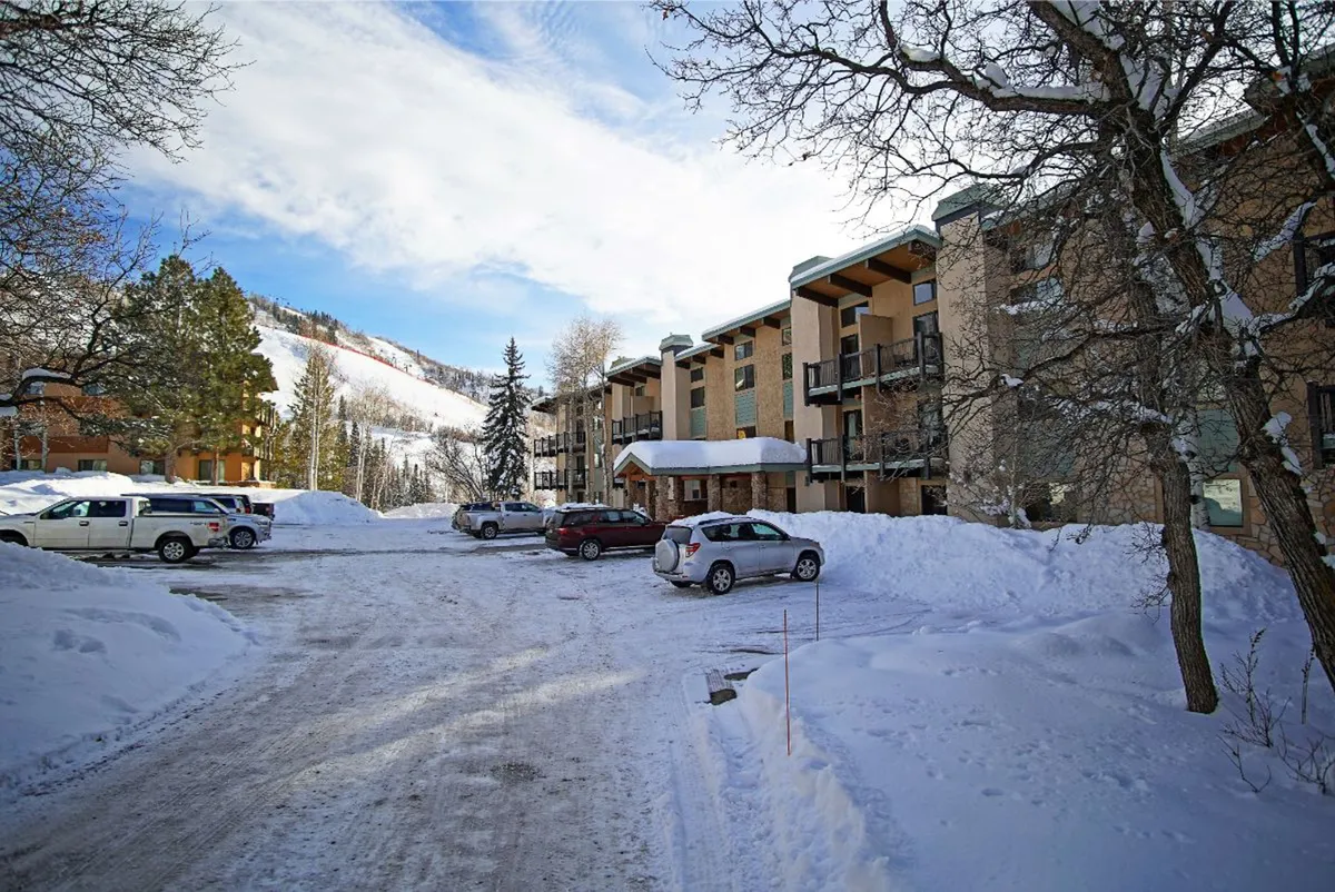 This exterior shot features the apartment building in a winter setting with parked cars and a clear mountain backdrop. The image captures the ease of parking and hints at the cozy retreat awaiting inside after time outdoors.