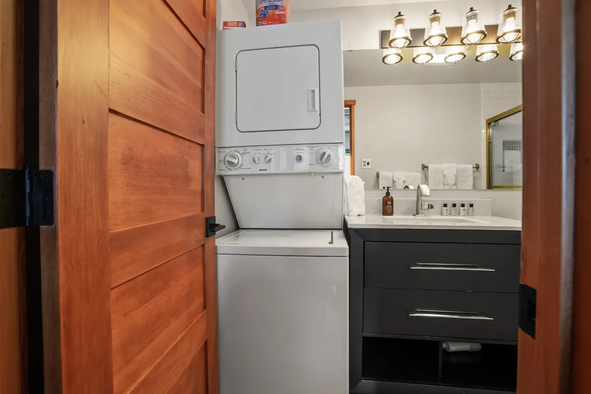 A practical yet inviting space featuring a washer and dryer set beside a bathroom vanity with a well-lit mirror. The design highlights the convenience of in-unit laundry while maintaining a clean and organized look.