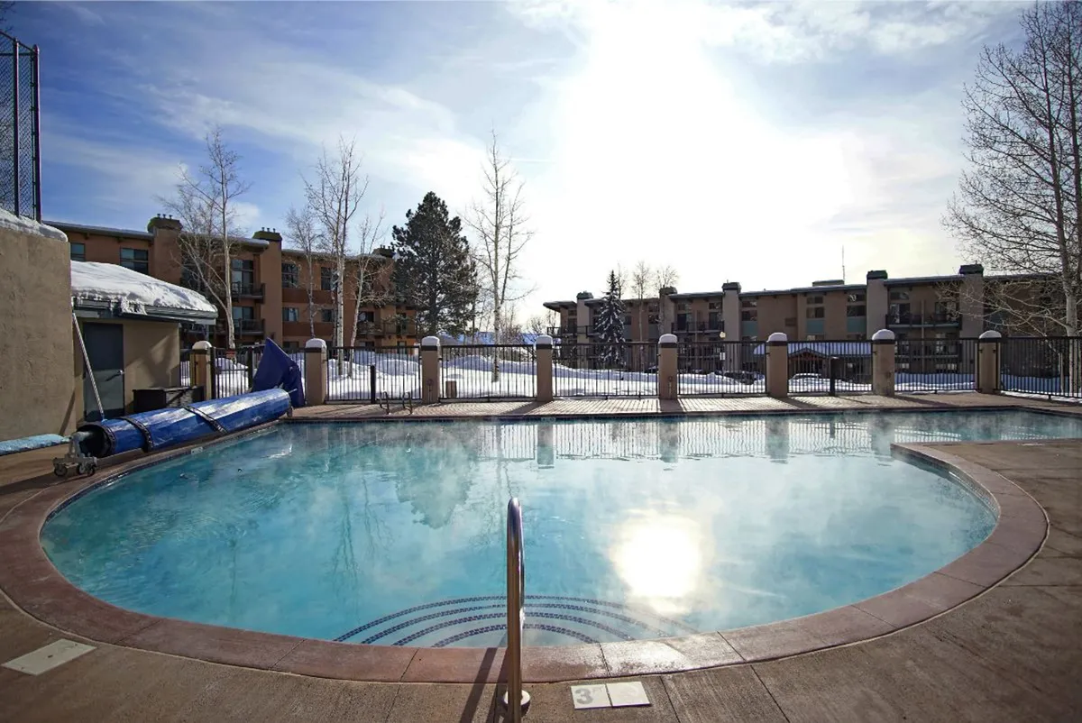 An inviting exterior view of the clubhouse swimming pool bordered by trees and residential buildings. The area is ideal for summer activities, with plenty of space for swimming, sunbathing, and relaxing with friends or family.